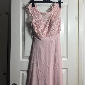 Ljusrosa spetsklänning från bpc - Supersöt ljusrosa långklänning från bpc selection premium. Överdelen är dekorerad med blommig spets och har breda axelband. Kjolen är slät och faller fint. Perfekt för vår och sommar, och materialet känns lätt och luftigt. Endast använd en gång💞
