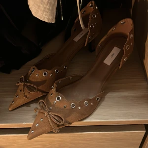 Bruna ballerinaskor med nitar från Nelly - Snygga bruna ballerinaskor från Nelly i mocka med spetsig tå, låg klack och silverfärgade nitar. 