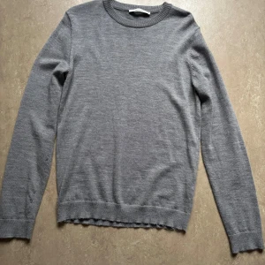 Grå stickad tröja från A Day's March - Säljer en stilren grå stickad tröja från A Day's March i storlek S. Tröjan har rund halsringning, ribbade muddar och är långärmad. Tröjan sitter på en 185 snubbe ca 75 kg, Nypris 600