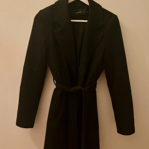 Vero Moda kappa - Svart kappa från Vero Moda i klassisk modell med krage och bälte i midjan. 