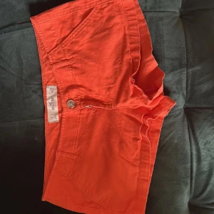 Röda shorts från Hollister - Snygga röda shorts från Hollister med klassisk passform och diskret logga broderad på fickan. Shortsen har knapp och dragkedja framtill, samt flera fickor. Perfekta för varma dagar och chill stunder. Materialet är mjuk bomull som känns skönt mot huden.