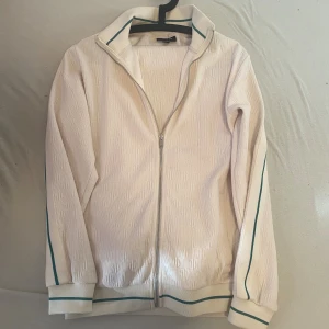 Vita mjukisbyxor med gröna detaljer - Säljer ett par vita mjukisbyxor från Only med gröna ränder längs sidorna och midjan. Byxorna har snörning i midjan och är tillverkade i ett mjukt, strukturerat material. Perfekta för en chill och sportig look.