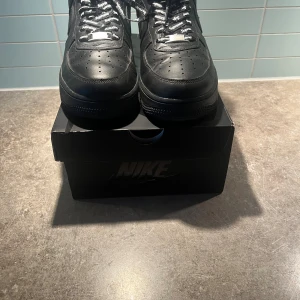 Nike Air Force 1 Supreme svart 42 - Säljer ett par svarta Nike Air Force 1 Low Supreme med Supreme-logga på sidan och specialdesignade svarta skosnören med Supreme-tryck. Skorna är i skinn och har klassisk rund tå och platt sula. Riktigt clean och stilren sneaker för dig som gillar streetwear. Ny pris 3499kr