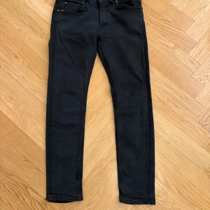 Svarta jeans från Tiger of Sweden, 32/32 - Svarta jeans från Tiger of Sweden med klassisk femficksdesign och diskret logga på bakfickan. Jeansen har smal passform och raka ben, tillverkade i mjukt bomullsmaterial med stretch för extra komfort. Perfekta för en stilren och modern look. 