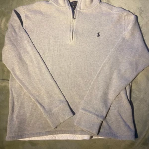 Polo Ralph Lauren grå half zip - Snygg grå långärmad tröja från Polo Ralph Lauren med half zip och klassisk broderad logga på bröstet. Tröjan är i mjuk bomull och har ribbade muddar vid ärmslut och nederkant. Perfekt för en chill och stilren look. Barnstorlek XL.