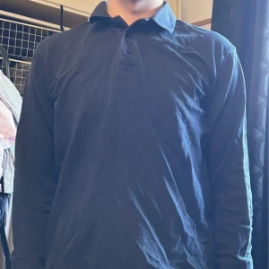 Mörkblå långärmad pikétröja - Snygg mörkblå pikétröja med klassisk krage och knappar framtill. Tröjan har lång ärm och är tillverkad i mjukt bomullsmaterial som känns skönt mot huden. Enkel och stilren design som funkar till många olika looks. Perfekt för dig som gillar en clean och chill stil.