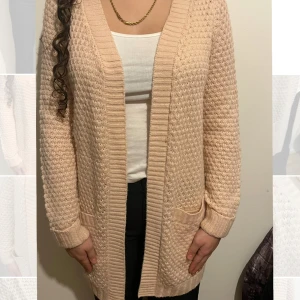 Ljusrosa stickad kofta med fickor - Mysig beige stickad kofta med lång ärm och två praktiska fickor framtill. Koftan har ett snyggt strukturerat mönster och breda ribbade kanter vid öppning, ärmslut och nederkant. Den är ljusrosa/ ljus aprikos i färgen . Knappt använd så ingen noppring eller liknande. Den är längre i modellen. 