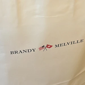 reserverad - Stor och rymlig shoppingväska i beige från Brandy Melville. Perfekt för att bära med sig allt man behöver under dagen. Väskan har tryckt logga med flaggor på framsidan och är tillverkad i ett slitstarkt material.