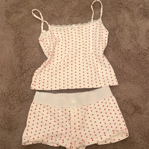 Vit linnetopp med röda hjärtan Gina Tricot - Supersöt vit linnetopp från Gina Tricot med tunna axelband och små röda hjärtan över hela tyget. Toppen har spetskant och en liten rosett framtill. Perfekt för dig som gillar gulliga detaljer och mjuka material.