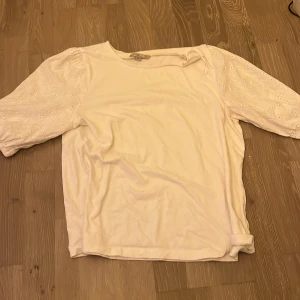 Vit blus med broderade puffärmar - Säljer en söt vit blus med puffiga kortärmar som har broderade blommor och hålmönster. Blusen har rund hals och är gjord i mjuk bomull. Perfekt för dig som gillar romantiska detaljer och vill ha en fräsch look.