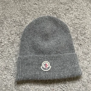Grå stickad Moncler mössa - Snygg grå stickad mössa från Moncler med klassisk uppvikt kant och broderad logotyp framtill. Säljer den då den inte kommit till så mycket andvändning, priset är förhandlingsbart!