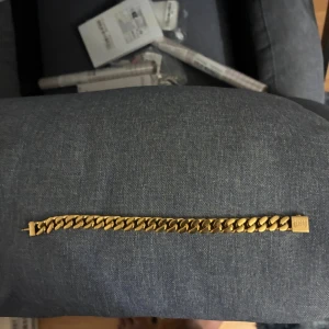 Guldigt kedjearmband från Blissi - Snyggt kedjearmband i guldplaterat från kejsar. Armbandet har breda, platta länkar som ger en cool och modern vibe. Perfekt för dig som gillar statement-smycken och vill sticka ut lite extra. Längden är 18 cm .