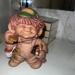 Fixar Trollet Jie Keramik - Charmig keramikfigur 'Fixar Trollet' designad av Eva Järnskog för Jie Keramik. Fint skick, handmålad med detaljer som verktyg och grön keps. Perfekt för samlare eller som dekorativ inredningsdetalj.