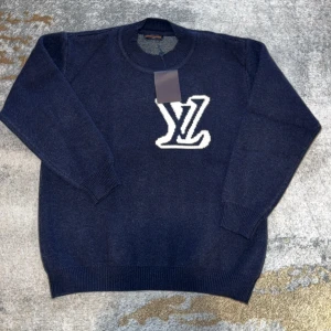 Mörkblå stickad tröja Louis Vuitton - Mörkblå stickad tröja från Louis Vuitton med stort vitt LV-logo på både fram- och baksidan. Tröjan har rund halsringning, ribbade muddar och är långärmad. Perfekt för dig som vill ha en lyxig och stilren look.