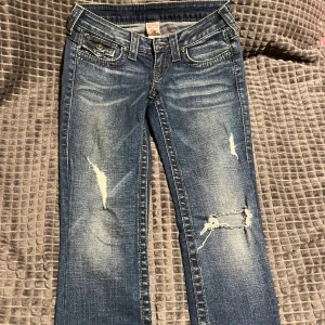 True Religion blå slitna jeans, stl 26 - Säljer ett par snygga blå jeans från True Religion i storlek 26 (motsvarar ca EU 34/XS). Jeansen har låg midja, raka ben och snygga slitningar med hål på benen samt öppningar vid sidorna. Använda endast en gång och i mycket fint skick!