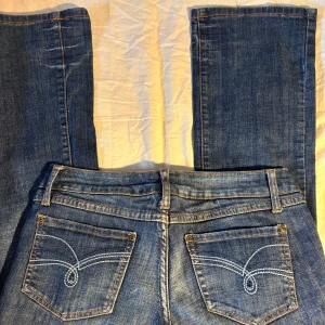 Blå Levi's 725 bootcut jeans - Säljer ett par blå lågmidjade 725 jeans med bootcut passform. Snygga kontrastsömmar, klassiska bakfickor med broderad detalj och låg midja. Insidan av linningen har blommigt tyg. Perfekta för dig som gillar en tidlös jeanslook med lite extra edge.