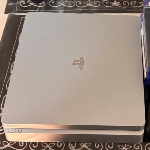 PlayStation 4 Slim - Snygg PlayStation 4 Slim i silver med tillhörande handkontroll och flera PS4-spel, inklusive Jump Force. Konsolen har några mindre ytliga repor men är i gott skick och fungerar utmärkt för gaming. Perfekt paket för dig som vill komma igång direkt! Pris kan diskuteras!