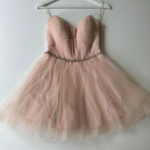 Ljusrosa kort klänning med rosett - Superfin ljusrosa kort klänning med axelbandslös design. Midjan är dekorerad med glittriga stenar för extra wow-känsla. Nyskick