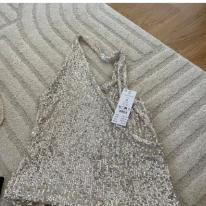 Glittrig silver paljett-topp från Gina Tricot - Säljer en glittrig silverfärgad topp från Gina Tricot, täckt med paljetter. Toppen har smala axelband och är ärmlös med en croppad passform. Perfekt för att sticka ut på festen eller nyår. Supersnygg att styla med höga jeans eller kjol.