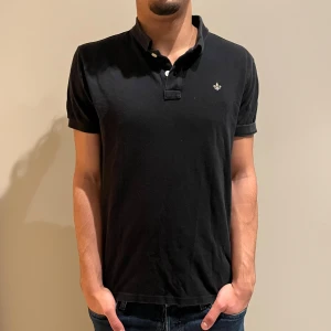 Svart piké från Morris  - Svart pikétröja från Morris Stockholm med klassisk krage och korta ärmar. Tröjan har två knappar vid halsen och en liten broderad logga på bröstet. Perfekt för en clean och stilren look. NYPRIS:1499Kr MITT PRIS:329 ✅