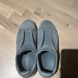 Grå sneakers från Axel Arigato mocka - Snygga grå sneakers från Axel Arigato i mocka med elastisk panel över vristen för enkel påtagning. Skorna har en vit platt sula med tydlig Arigato-logga undertill och en stilren, minimalistisk design. Perfekta för dig som gillar en clean och modern look. Köpt från nk, har kvitto o allt. Tar emot byten (valentino open helst)