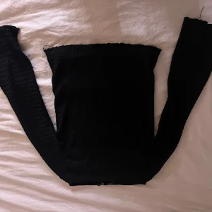 Svart offshoulder topp med struktur - Säljer en svart offshoulder topp med lång ärm och snygg strukturerad yta. Toppen är tight och croppad, perfekt att styla med höga jeans eller kjol. Enkel men ändå trendig design som passar till många olika looks.