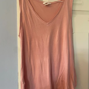 Rosa ärmlös linnetopp från H&M - Säljer en enkel och snygg rosa linnetopp från H&M Basic. Toppen är ärmlös med v-ringning och har en mjuk, tunn känsla. Perfekt att matcha med jeans eller kjol för en chill look.