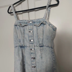 Ljusblå jeansklänning från FB Sister - ⚠️ Skriv till mig innan köp!⚠️Säljer en snygg ljusblå jeansklänning från FB Sister i storlek M. Klänningen har knappar framtill, smala axelband och dragkedja i sidan som är lite trög ibland. Den har en cool tvättad denimlook och markerad midja som ger en trendig siluett.
