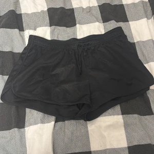 Svarta sportshorts från H&M - Svarta sportiga shorts från H&M Sport i storlek M. De har en klassisk loose passform, elastisk midja med snörning och är tillverkade i lätt polyester. Perfekta för träning eller chill dagar när du vill ha det bekvämt.