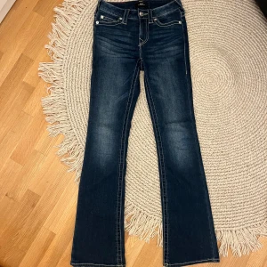 True Religion Bootcut Jeans becca - Snygga mörkblå jeans från True Religion i modellen Becca Mid Rise Bootcut. Klassisk femficksdesign med kontrastsömmar och ikonisk broderad logga på bakfickorna. Jeansen har medelhög midja och är tillverkade i slitstarkt denim.