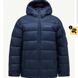 Mörkblå dunjacka Peak Performance - Säljer en mörkblå dunjacka från Peak Performance med huva och dragkedja. Jackan är quiltad och har en clean, sportig look med logga på bröstet. Perfekt för kalla dagar och riktigt skön att bära. Passformen är normal och jackan har långa ärmar. Super bra skick, pris kan diskuteras. Nypris: 4200kr
