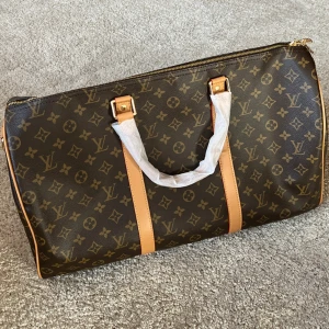 Louis Vuitton weekendbag monogram - Säljer en klassisk Louis Vuitton weekendbag i brunt och svart med ikoniskt monogrammönster. Väskan har detaljer i skinn, guldfärgade metalldelar och dragkedja. Perfekt storlek för resor och har både handtag och fästen för axelrem.