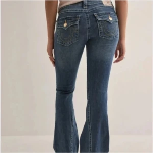 Blå bootcut jeans från True Religion - Snygga blå bootcut jeans från True Religion med klassiska kontrastsömmar och guldiga knappar på bakfickorna. Jeansen har låg midja och är tillverkade i jeansmaterial med en lätt utsvängd passform nertill. Perfekta för dig som gillar en retroinspirerad look. Aldrig använda, storlek 27💕
