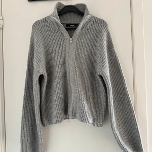 Grå stickad kofta från BikBok - Mysig grå stickad kofta från BikBok i storlek XS. Koftan har grov ribbstickning, hög krage och hel dragkedja framtill. 