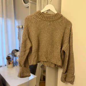 Beige stickad croppad tröja - Mysig beige stickad tröja med croppad passform och bred polokrage. Tröjan har långa ärmar med uppvikta muddar och grovstickad struktur som ger en avslappnad vibe, perfekt till hösten! 