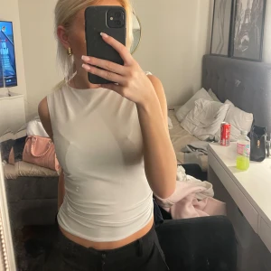 Vit ärmlös linnetopp - Säljer en stilren vit ärmlös linnetopp med hög halsringning. Toppen sitter tight mot kroppen, perfekt att matcha med jeans eller kjol. Materialet känns mjukt och stretchigt, vilket gör den superbekväm. Använd fåtal ggr, nypris 200kr