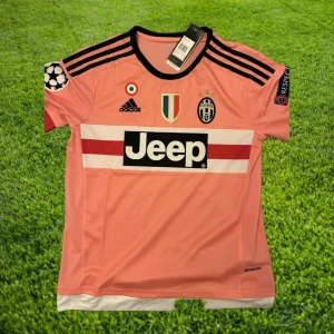Pogba - Juventus 15/16  - Helt oanvänd/nyskick Paul Pogba Juventus bortatröja från säsongen 2015/2016. Den fina rosa färgen plus Pogbas otroliga säsong har gjort tröjan ikonisk bland dagens retrotröjor! Tveka inte med att höra av er för mer information eller frågor!