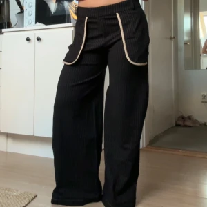 Svarta vida byxor beiga detaljer - Säljer ett par svarta vida kostymbyxor med tunna vita ränder och utefickor. Perfekta för en chill och trendig look. Bra skick