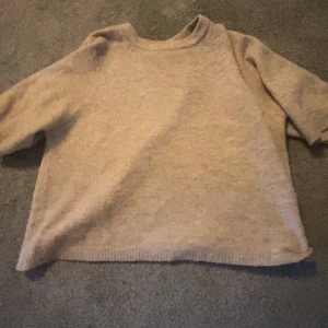 Beige stickad tröja med kort ärm - En enkel och stilren beige stickad tröja med korta ärmar och rund hals. Tröjan har en avslappnad passform och ribbade kanter vid hals och nederkant. Perfekt för lager-på-lager under kyliga dagar.