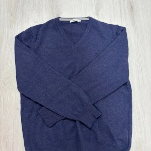 Merinoull stickad tröja från J.Lindeberg - Mörkblå stickad tröja från J.Lindeberg med v-ringad hals och fullt gjord av merino ull och diskret JL-logga på bröstet. Tröjan har långa ärmar och ribbade muddar vid ärmslut och nederkant. Perfekt för lager-på-lager under kyliga dagar. Storlek L men sitter som S skulle jag säga 