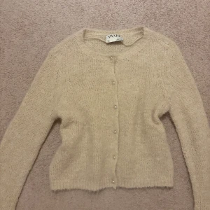 Stickad kofta - Supermjuk och fluffig beige stickad kofta från AWARE. Koftan har rund halsringning, långa ärmar och pärlknappar framtill. Perfekt för lager-på-lager och ger en chill men ändå söt vibe till din outfit. Aldrig använd