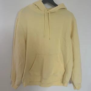 Gul hoodie från H&M, relaxed fit - Ljusgul hoodie från H&M i relaxed fit med huva och dragsko. Tröjan har en stor magficka och ribbade muddar vid ärmslut och nederkant. Perfekt för chill dagar och enkel att matcha med jeans eller mjukisbyxor.