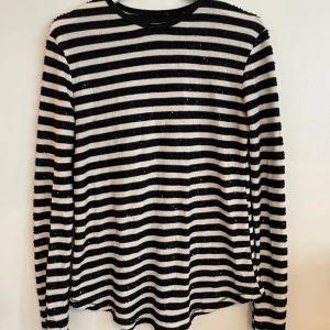 Randig svartvit paljett-tröja - Svart och vit långärmad tröja med horisontella ränder och svarta paljetter på de svarta ränderna. Tröjan har rund halsringning och är i ett mjukt, stretchigare material. 