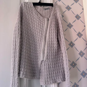 Beige stickad kofta från Hunkydory - Säljer en beige stickad kofta från Hunkydory Essentials. Koftan har grovstickat mönster, lång ärm och en sned dragkedja framtill. Tillverkad i bomull, perfekt för lager-på-lager under höst och vår. Enkel och stilren design som passar till det mesta.