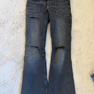 Bootcut jeans från Gina Tricot, stl 152 - Mörkgrå bootcut jeans från Gina Tricot med slitna detaljer och hål vid knäna. Jeansen har stora fickor fram och är tillverkade i klassiskt denimtyg. Perfekt för dig som gillar en avslappnad och trendig look. Det är något märke när dom knät men annars väldigt bra skick.