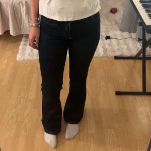 Mörkblå bootcut jeans  - Säljer ett par mörkblå jeans med bootcut-modell. Jeansen har klassiska fickor både fram och bak, samt tydliga kontrastsömmar. Materialet är jeans och passformen är normal med lite utsvängda ben nertill.