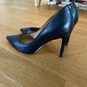 Svarta pumps från Sam Edelman - Klassiska svarta pumps från Sam Edelman i skinn med spetsig tå och hög klack. Snygg och tidlös modell som passar till många olika outfits. Insidan har logotyp i guld. Perfekta för dig som vill ha en elegant, vintage och stilren sko.