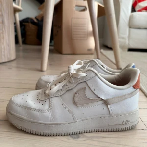 Nike Air Force 1 LX Vandalised  - Nike Air Force 1 sneakers i vitt skinn med klassisk siluett och snörning. Swoosh-loggan är i mocka och skorna har färgade innersulor, en röd och en blå, samt detaljer i samma färger på hälen. Perfekta för dig som gillar en clean och stilren look. Gott skick, köpt i Kanada, kan skickas eller hämtas :)