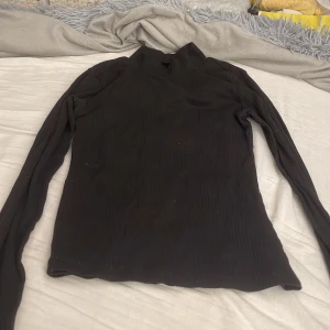 Svart ribbad polotröja från H&M - Svart ribbad polotröja från H&M med lång ärm och tight passform. Perfekt att styla med jeans eller kjol för en clean look. Hög krage och stretchigt material gör den både bekväm och snygg.