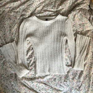 Vit ribbad stickad tröja - Supermjuk och ribbad stickad tröja från H&M i vitt. Tröjan har lång ärm, rund halsringning och en slim passform som sitter snyggt. Perfekt att styla med jeans eller kjol för en chill look. Litet hål framtill, se andra bilden.